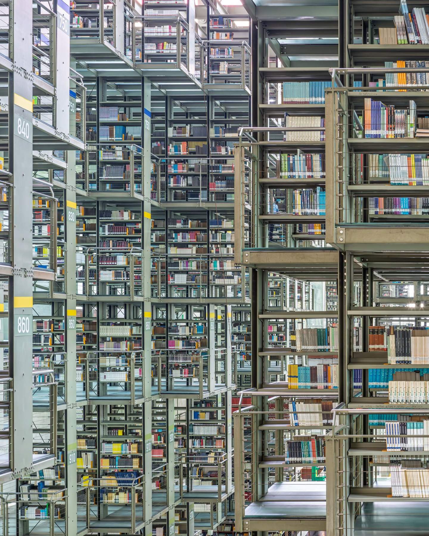 Biblioteca Vasconcelos suspended book stacks seen from below, teal-green glass walkway platforms catching diffuse light between levels